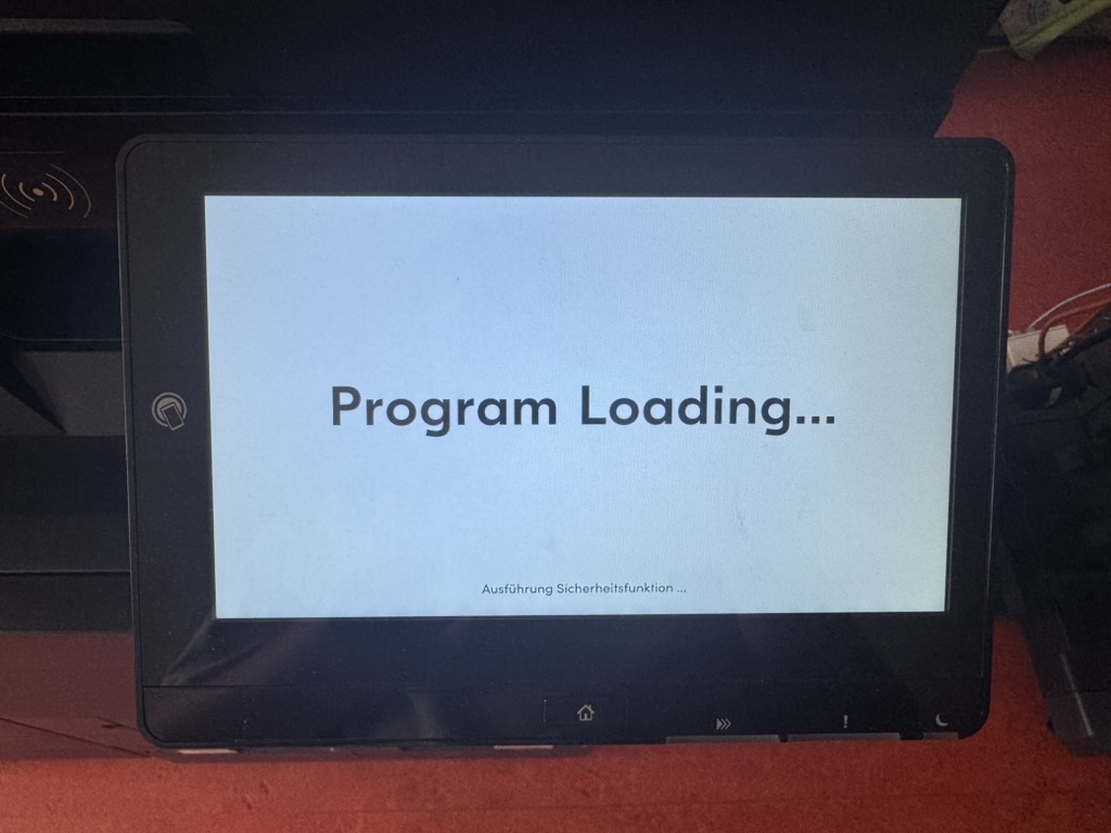 Touchscreen des Geräts mit der Anzeige „Program Loading…“ und dem Hinweis „Ausführung Sicherheitsfunktion“